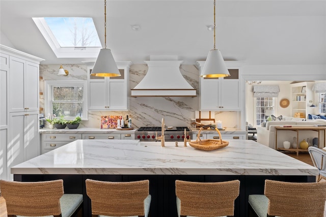 kitchen with tasteful backsplash, an island with sink, hanging light fixtures, and custom range hood