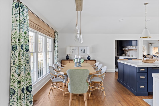 dining area with vaulted ceiling, sink, and light hardwood / wood-style flooring