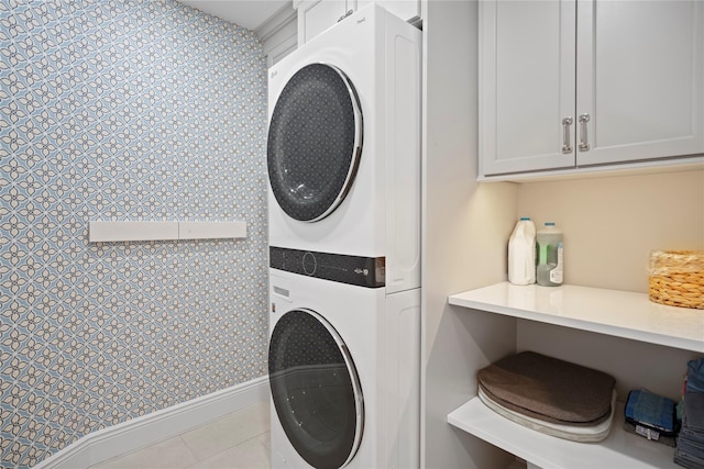 laundry room featuring stacked washer / dryer, light tile patterned floors, and cabinets