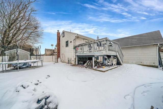 snow covered house featuring a trampoline and a deck