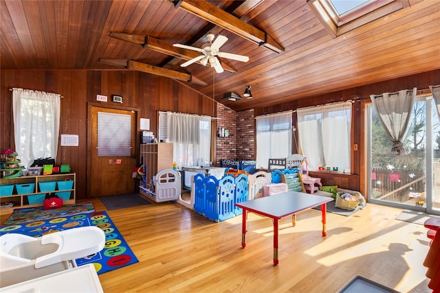 playroom featuring lofted ceiling with skylight, wooden walls, light hardwood / wood-style floors, and a healthy amount of sunlight