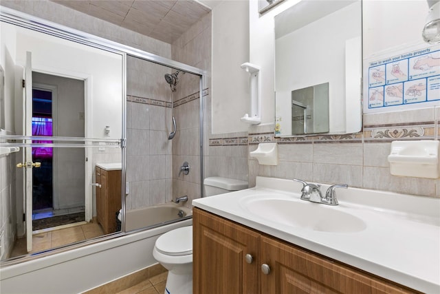 full bathroom featuring combined bath / shower with glass door, tile walls, tile patterned flooring, vanity, and toilet