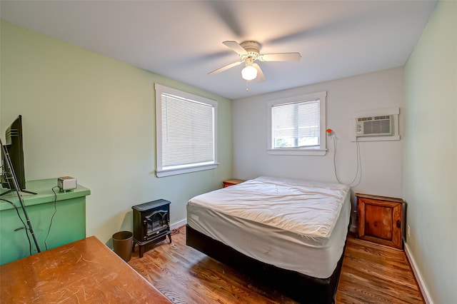 bedroom with hardwood / wood-style flooring, a wood stove, a wall mounted air conditioner, and ceiling fan