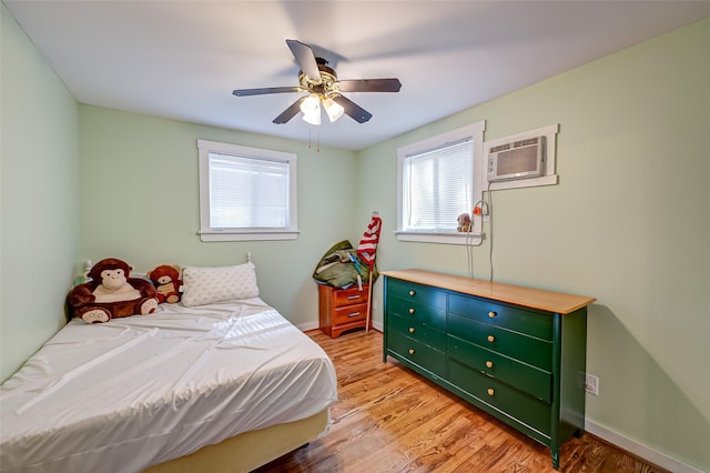 bedroom with a wall mounted air conditioner, light hardwood / wood-style flooring, and ceiling fan