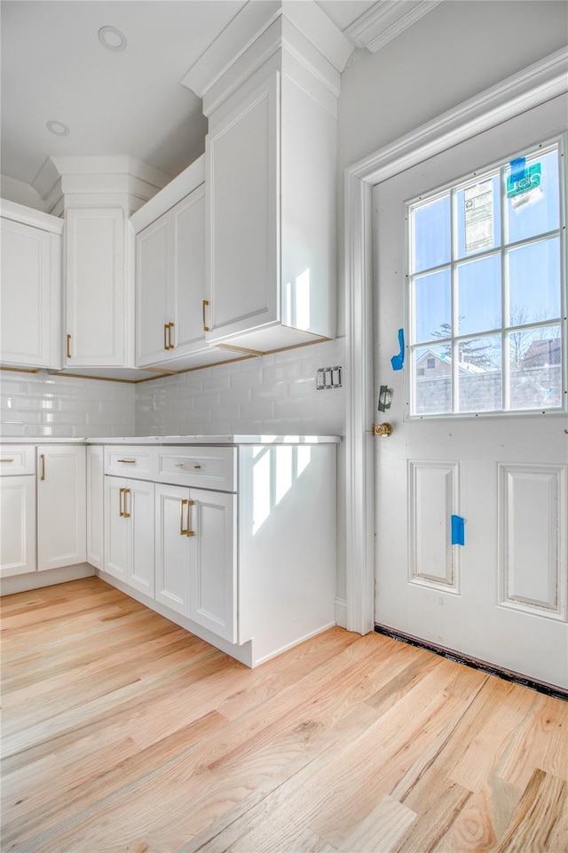 interior space with tasteful backsplash, ornamental molding, white cabinets, and light hardwood / wood-style flooring