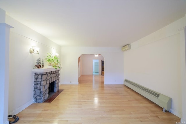 living room with an AC wall unit, light wood-type flooring, a stone fireplace, and baseboard heating