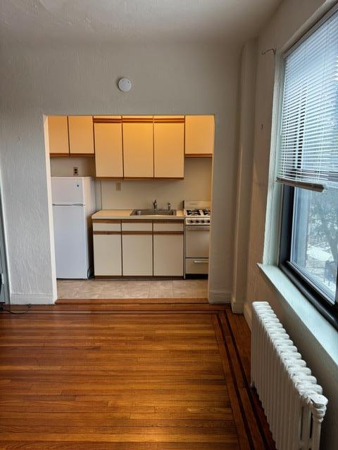 kitchen featuring radiator, sink, white appliances, and light wood-type flooring