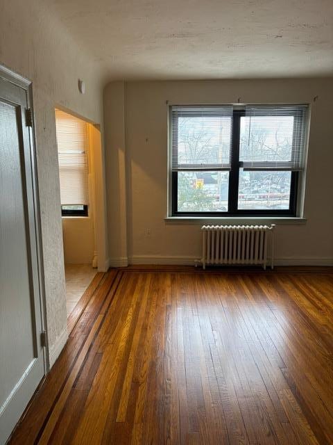 unfurnished room with dark wood-type flooring and radiator heating unit