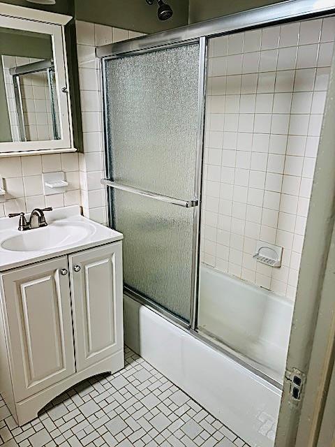 bathroom with tile patterned floors, tasteful backsplash, bath / shower combo with glass door, tile walls, and vanity