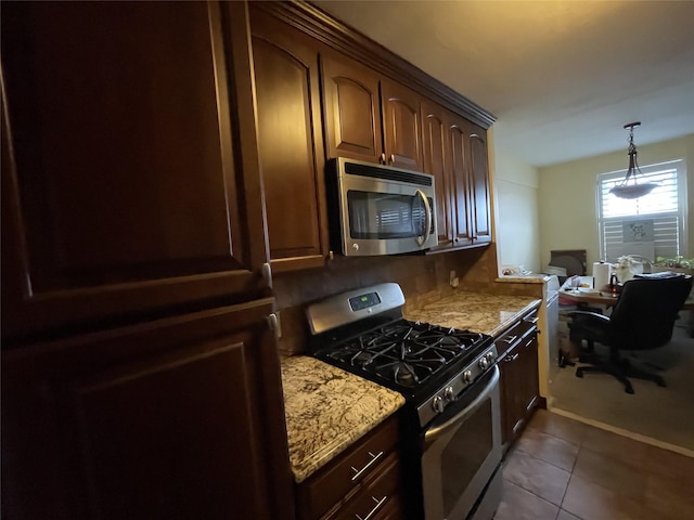 kitchen featuring light stone counters, dark tile patterned flooring, decorative light fixtures, and appliances with stainless steel finishes