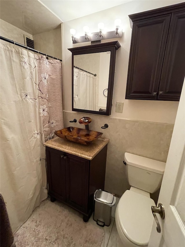 bathroom with vanity, toilet, a shower with shower curtain, and tile walls