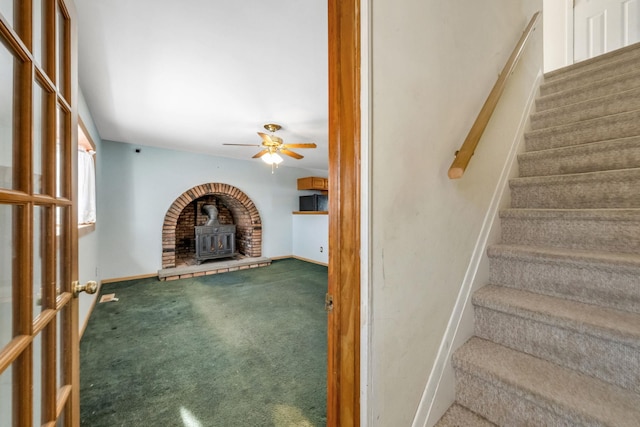 unfurnished living room with ceiling fan, carpet flooring, and a wood stove