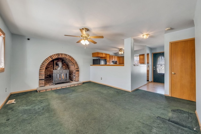 unfurnished living room with light colored carpet, ceiling fan, and a wood stove