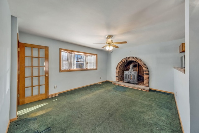 unfurnished living room with ceiling fan, carpet floors, and a wood stove