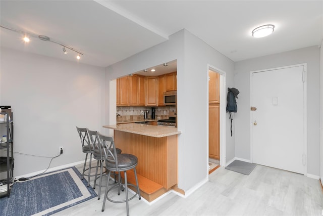 kitchen with light hardwood / wood-style floors, stainless steel appliances, kitchen peninsula, a breakfast bar area, and tasteful backsplash