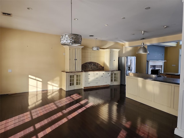 kitchen featuring dark wood-type flooring, backsplash, stainless steel fridge, pendant lighting, and cream cabinetry