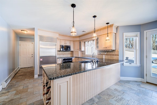 kitchen featuring sink, dark stone countertops, a baseboard radiator, kitchen peninsula, and stainless steel appliances