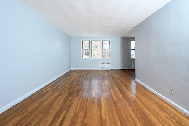 empty room with radiator heating unit and dark hardwood / wood-style flooring