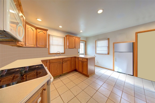 kitchen featuring tasteful backsplash, light countertops, a sink, white appliances, and a peninsula