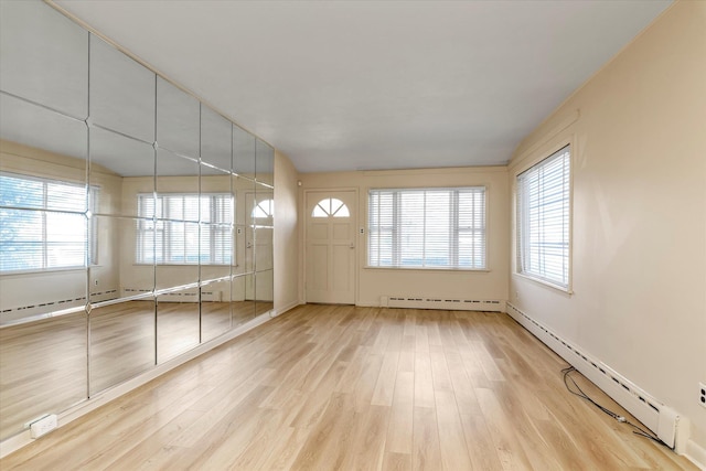 spare room featuring a baseboard radiator, light hardwood / wood-style floors, and a healthy amount of sunlight