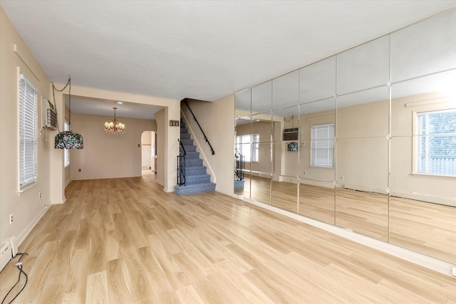 unfurnished living room with an AC wall unit, an inviting chandelier, and light hardwood / wood-style flooring