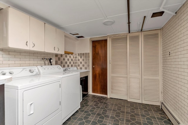 laundry area with cabinets, brick wall, washing machine and clothes dryer, and a baseboard heating unit