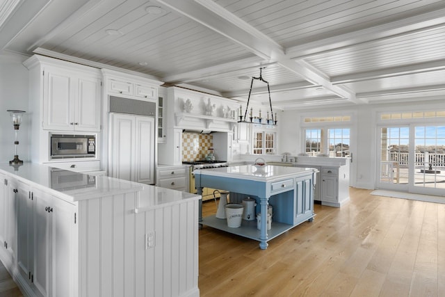 kitchen with white cabinetry, a center island, built in appliances, decorative light fixtures, and beamed ceiling