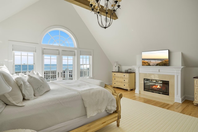 bedroom with lofted ceiling with beams, a water view, a fireplace, and light hardwood / wood-style flooring