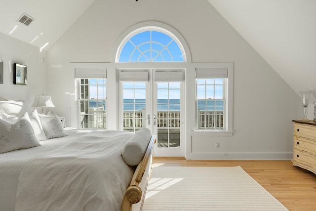 bedroom featuring vaulted ceiling, access to outside, a water view, light wood-type flooring, and french doors