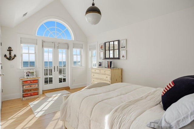 bedroom with french doors, a water view, vaulted ceiling, light wood-type flooring, and access to exterior