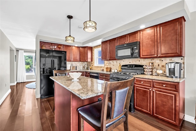 kitchen with hanging light fixtures, black appliances, light stone countertops, and a kitchen island