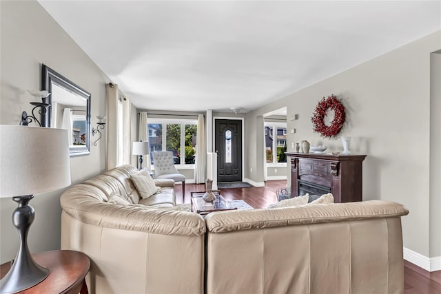 living area featuring baseboards, dark wood-style flooring, and a glass covered fireplace