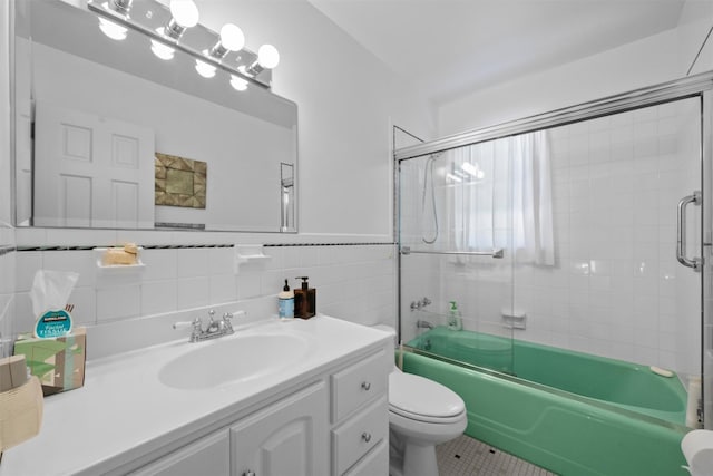 full bathroom with shower / bath combination with glass door, tile walls, tile patterned flooring, vanity, and toilet