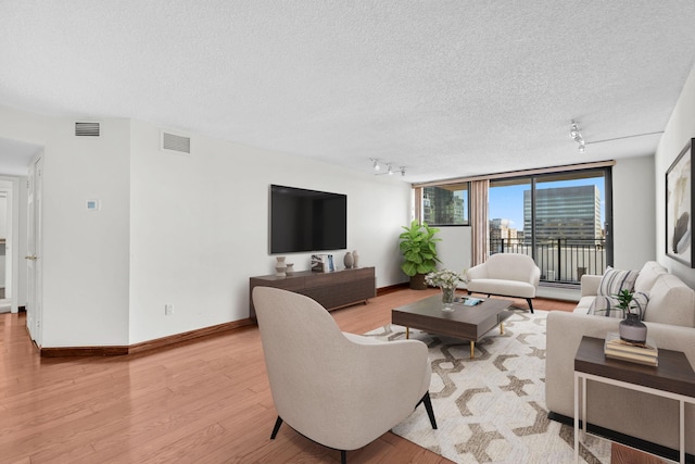 living room with rail lighting, visible vents, light wood finished floors, and a textured ceiling