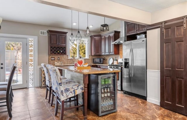 kitchen with a breakfast bar, appliances with stainless steel finishes, a center island, wine cooler, and decorative light fixtures