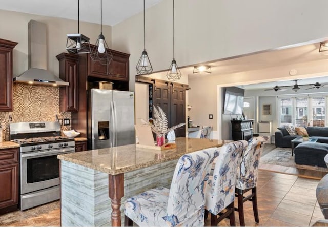 kitchen featuring appliances with stainless steel finishes, backsplash, hanging light fixtures, a center island, and wall chimney range hood