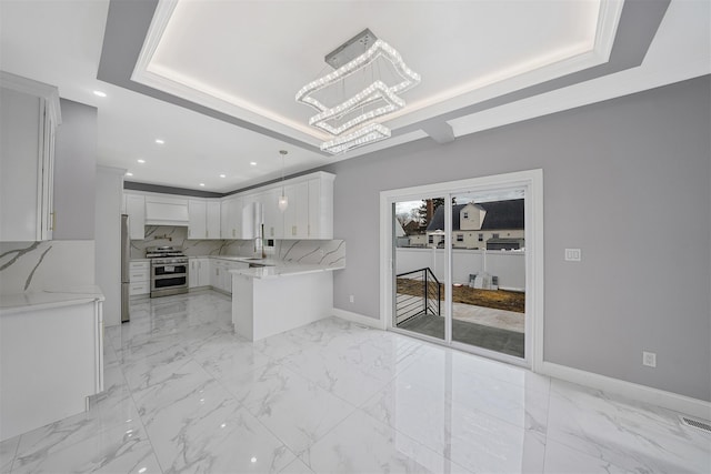 kitchen with decorative light fixtures, appliances with stainless steel finishes, a tray ceiling, light stone countertops, and white cabinets