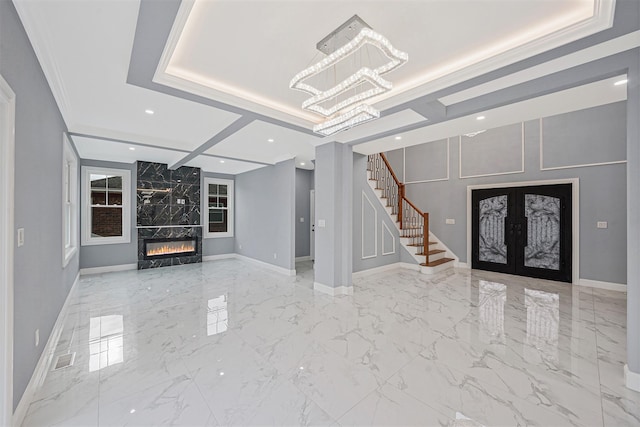 unfurnished living room featuring a tray ceiling, a premium fireplace, ornamental molding, and french doors