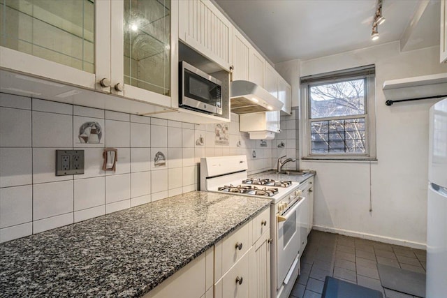 kitchen with backsplash, dark stone counters, white gas stove, and white cabinets