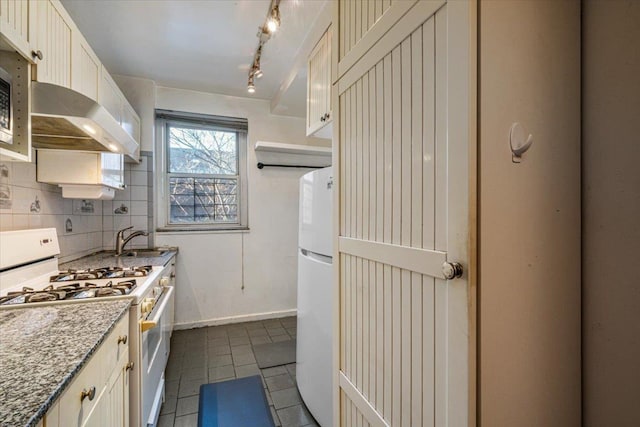 kitchen featuring sink, dark tile patterned floors, white appliances, light stone countertops, and decorative backsplash