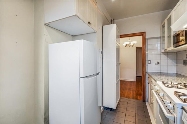 kitchen with backsplash, dark tile patterned flooring, a notable chandelier, light stone counters, and white appliances