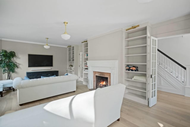 living room with crown molding, light wood-type flooring, built in features, and a fireplace