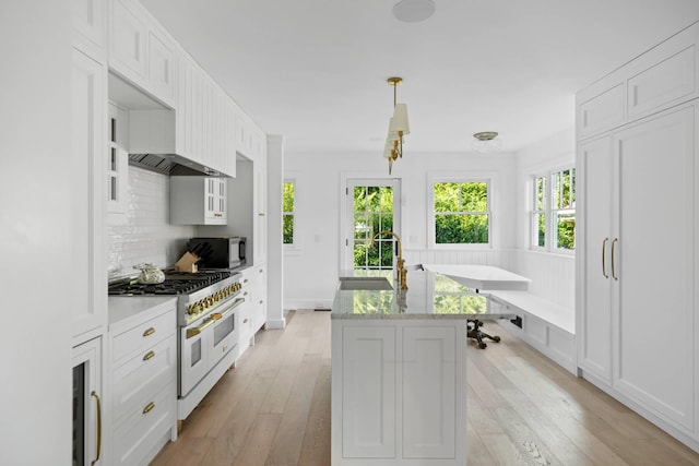 kitchen featuring sink, backsplash, range with two ovens, white cabinets, and light wood-type flooring