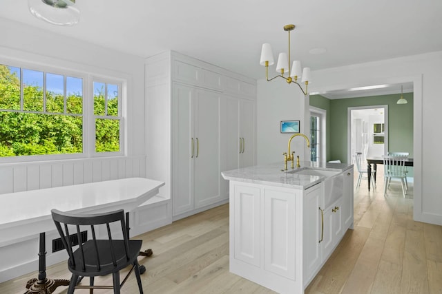 kitchen with pendant lighting, white cabinetry, light stone counters, a center island with sink, and breakfast area