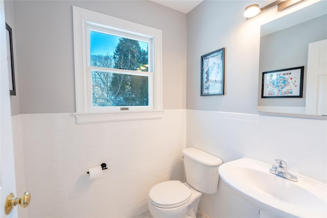 half bath featuring tile walls, toilet, a wainscoted wall, and a sink