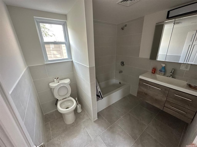 full bathroom featuring toilet, tile walls, vanity, tiled shower / bath combo, and tile patterned flooring