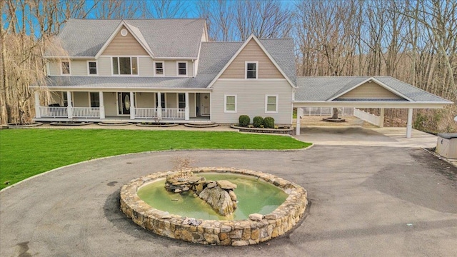 view of front of house with curved driveway, covered porch, a small pond, and a front lawn