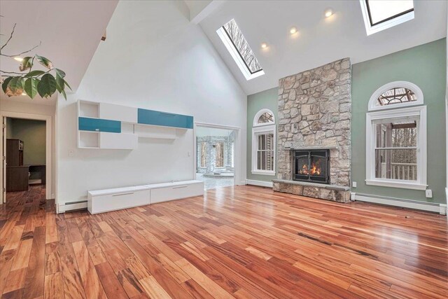 unfurnished living room featuring baseboard heating, wood finished floors, a skylight, high vaulted ceiling, and a baseboard heating unit