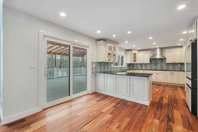 kitchen with a peninsula, visible vents, wall chimney exhaust hood, and light wood-type flooring
