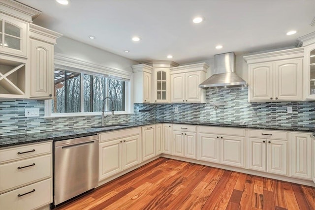 kitchen with light wood-style flooring, a sink, wall chimney range hood, backsplash, and stainless steel dishwasher